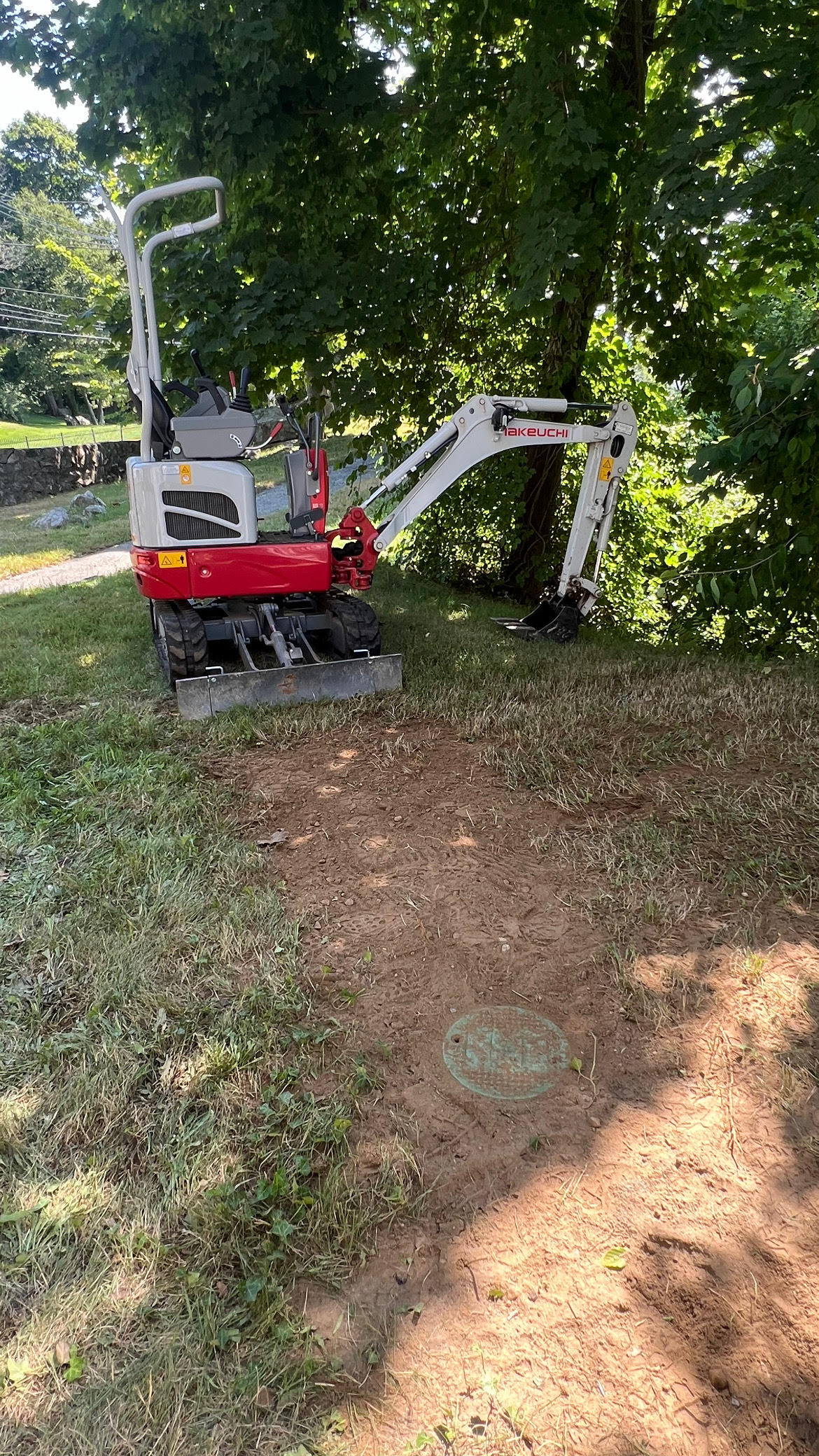 Photo of an excavator parked near a newly installed sewer cleanout on a grassy area.